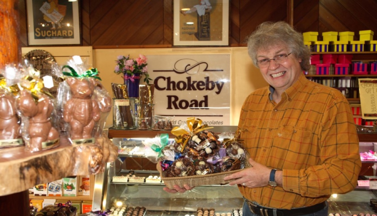The founder behind the counter of the Chokeby Road chocolate shop in the 1990s, surrounded by trays of handmade chocolates.