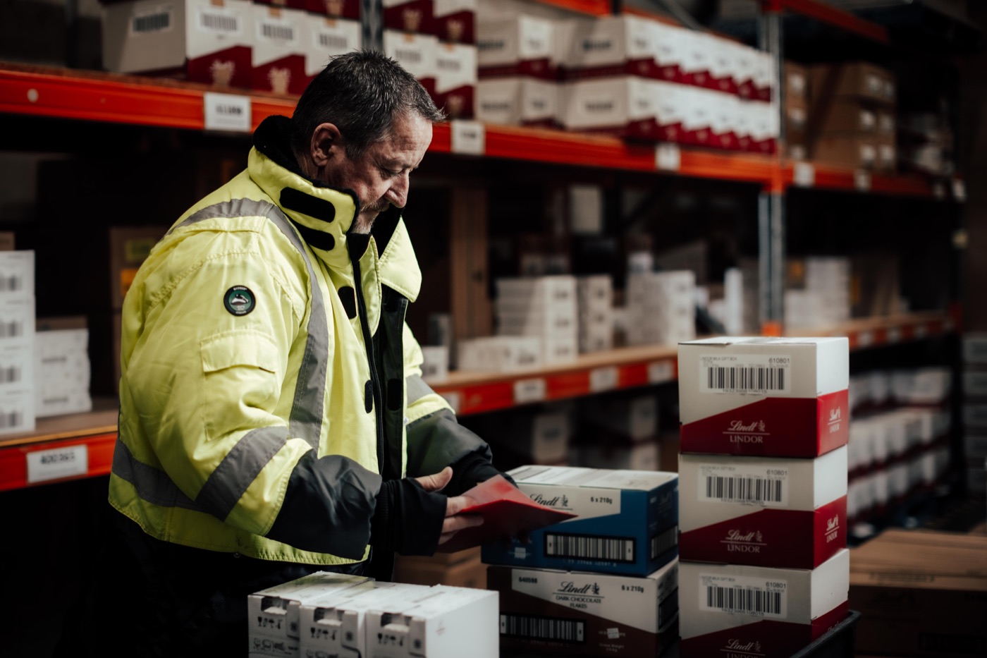 A warehouse team member in a hi-vis vest checking cartons stacked on a pallet in the cold store.